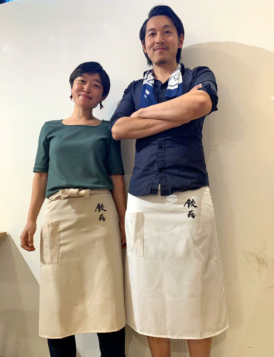 餃苑様の素敵なお２人の実際のエプロンユニフォームの着用写真です。<br>左の女性が着用されてるのがベージュ。右の男性はホワイトを着用！