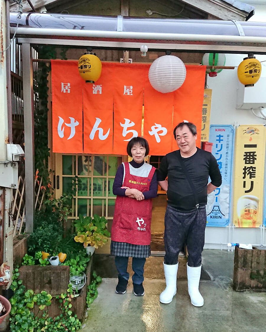 居酒屋けんちゃん様の新品のオレンジ色のオーダー暖簾と一緒に店主と奥様とを記念撮影させていただきました。<br>（弊社と同じ福知山市内の居酒屋さんなので私店長細見が納品いたしました！）<br>鮮やかなオレンジ色の暖簾が輝いてます♪<br>ちなみにオレンジ色は店主さんのラッキーカラーなのです！